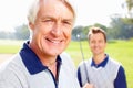 Senior man smiling. Closeup of senior man smiling with son holding a golf club in background. Royalty Free Stock Photo