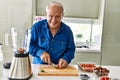 Senior man smiling confident cutting strawberry at kitchen