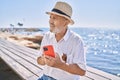 Senior man smiling confident wearing summer hat using smartphone at seaside Royalty Free Stock Photo