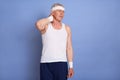 Senior man in sporty clothing, hairband and waistband, has injury, touching his pain neck, standing against blue wall, suffering Royalty Free Stock Photo