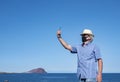 Senior man standing on cliff with straw hat using cellphone for a selfie enjoying freedom wearing face mask because of Royalty Free Stock Photo