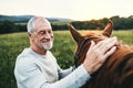 A senior man standing close to a horse outdoors in nature, stroking it. Royalty Free Stock Photo