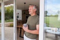 Senior Man Standing And Looking Out Of Kitchen Door Drinking Coffee Royalty Free Stock Photo