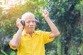 Senior man standing wearing wireless headphones listening to a favorite song, and smiling while standing in a garden. Royalty Free Stock Photo