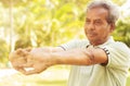 Senior man stretches hands before exercise - Concept of elderly person fitness outdoor - 60s person doing yoga asana at