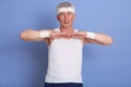 Senior man stretching hands indoors against blue background, warming up before training or playing tennis, mature male wearing Royalty Free Stock Photo