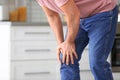 Senior man suffering from knee pain in kitchen, closeup.