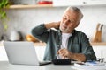 Senior Man Suffering Neckache While Working With Laptop In Kitchen Interior