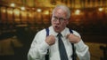Senior man in a suit gestures confidently while speaking inside a dimly lit church, emphasizing his points with expressive hand Royalty Free Stock Photo