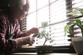 Senior man taking care of Japanese bonsai plant near window indoors. Creating zen atmosphere at home