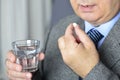 A senior man taking medicine with a glass of water.