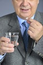 A senior man taking medicine with a glass of water.