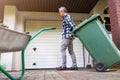 Senior man rolling garbage can