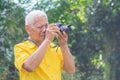 Senior man taking a photo by a digital camera in the park. An elderly Asian man wears a yellow shirt, happy when using a camera.