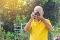 Senior man taking a photo by a digital camera while standing in the park. An elderly Asian man wears a yellow shirt be happy when