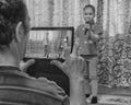 Senior man taking video of little Asian girl singing karaoke at home concert. Royalty Free Stock Photo