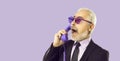 Senior man talking on landline phone with shocked and scared face isolated on purple background. Royalty Free Stock Photo