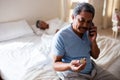 Senior man talking on mobile phone while looking at medicine in bedroom Royalty Free Stock Photo