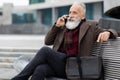 Senior man talking on phone, sitting on bench by office Royalty Free Stock Photo