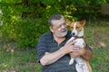 Senior man talking to his cute dog basenji taking it in the hands while resting in summer park Royalty Free Stock Photo