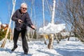Senior man throwing snow with shovel from private house yard in winter on bright sunny day. Elderly person removing snow in garden