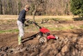 Senior man tilling ground soil with a rototiller in the garden.