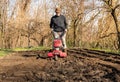 Senior man tilling ground soil with a rototiller in the garden.
