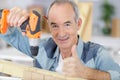 senior man using cordless screwdriver and holding thumbs up