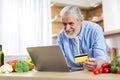 Senior Man Using Laptop And Credit Card In Kitchen, Ordering Groceries Online Royalty Free Stock Photo