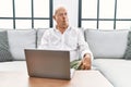 Senior man using laptop at home sitting on the sofa making fish face with lips, crazy and comical gesture Royalty Free Stock Photo
