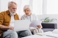 Senior man using laptop near wife with papers, calculator and notebook on table. Royalty Free Stock Photo