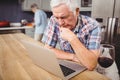 Senior man using laptop and woman working in kitchen Royalty Free Stock Photo