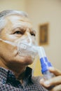 Senior man using medical equipment for inhalation with respiratory mask, nebulizer