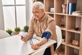 Senior man using tensiometer sitting on table at home