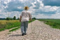 Senior man with walking stick wearing straw hat goes home on a cobblestone road Royalty Free Stock Photo