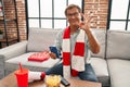 Senior man watching football looking at smartphone doing ok sign with fingers, smiling friendly gesturing excellent symbol