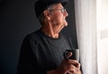 Senior Man Wearing Cap Relaxing Standing By Window At Home With Hot Drink Royalty Free Stock Photo