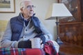 Senior Man Wearing Extra Clothes With Hot Drink Trying To Keep Warm At Home In Energy Crisis