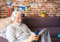 Senior man wearing headphones sitting on sofa and using mobile phone at home - retired, leisure and people concept Royalty Free Stock Photo