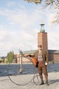 Senior man wearing old fashioned tweed suit holding a high wheeler bicycle in front of Stockholm City Hall Royalty Free Stock Photo