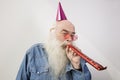 Senior man wearing party hat while blowing horn against gray background