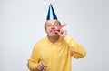 Senior man wearing party hat while blowing horn