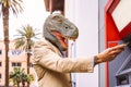 Senior man wearing t-rex dinosaur mask withdraw money from bank cash machine with debit card