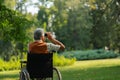 Senior man in wheechair spending free time outdoors in nature, watching forest animals through binoculars. Royalty Free Stock Photo