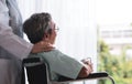 Senior man on a wheelchair alone in a room with doctor take care looking through the hospital window. Elderly patient