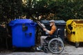 Senior man in wheelchair throwing paper waste, cardboard into recycling container in front his apartment. Elderly man