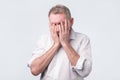 Senior man in white shirt covering his face with both hands Royalty Free Stock Photo