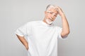 Senior man in white shirt and glasses looking puzzled, isolated on grey background