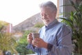 Senior man at the window holding a cup of coffee. Smiling bearded elderly man grey haired