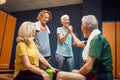 Senior man and woman high fiving in gym locker room, feeling energized for workout, mature woman and young woman cheering for them